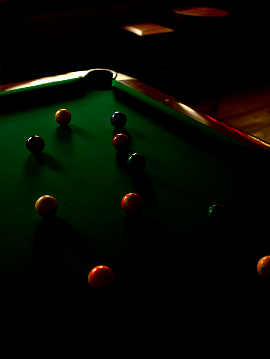 Several colorful billiard balls rest on a deep green felt pool table in a dimly lit bar setting