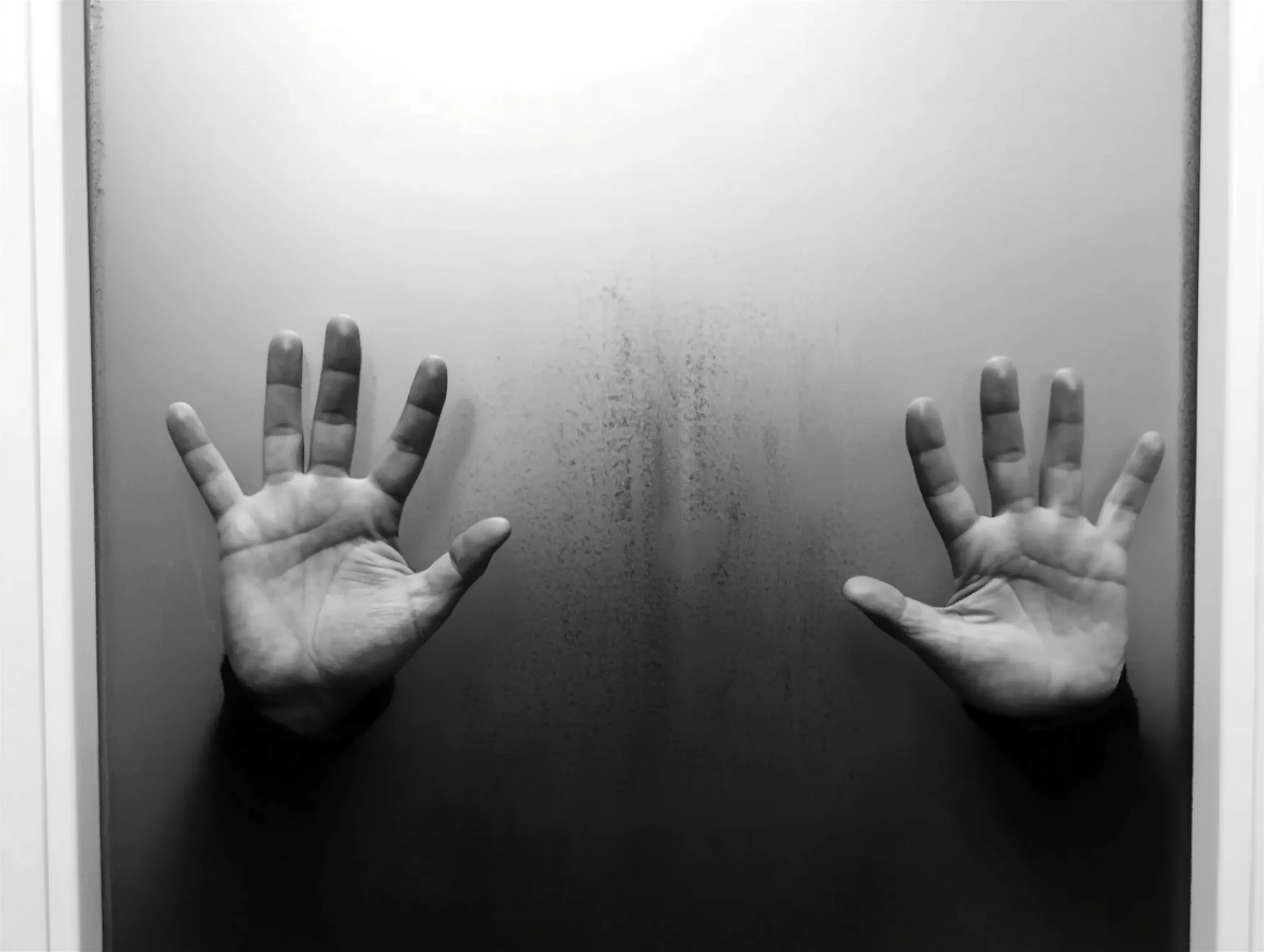 A black-and-white photography of two hands pressed against foggy glass